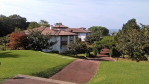 A white building with a tiled roof, surrounded by green lawns and trees.