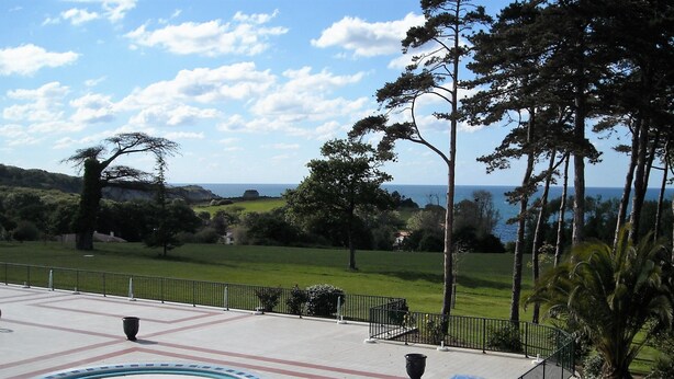 A park with a paved area, a view of the sea, and a grassy field.