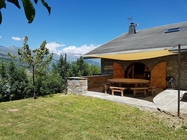 Un chalet avec une façade en pierre, une table et des bancs en bois, et une vue sur les montagnes.