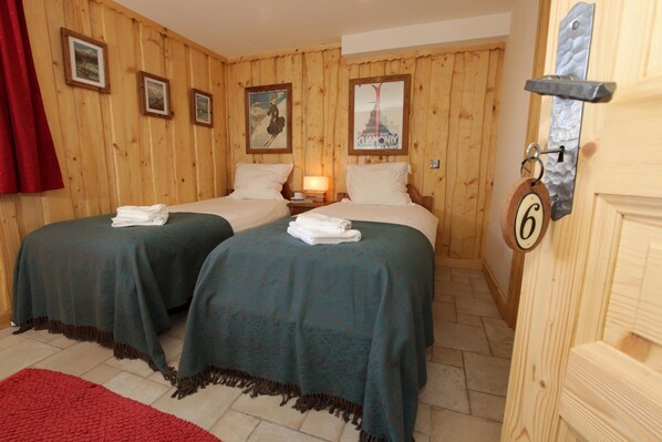 Una habitación con dos camas, paredes de madera, cuadros enmarcados, una cortina roja y una puerta con el número.