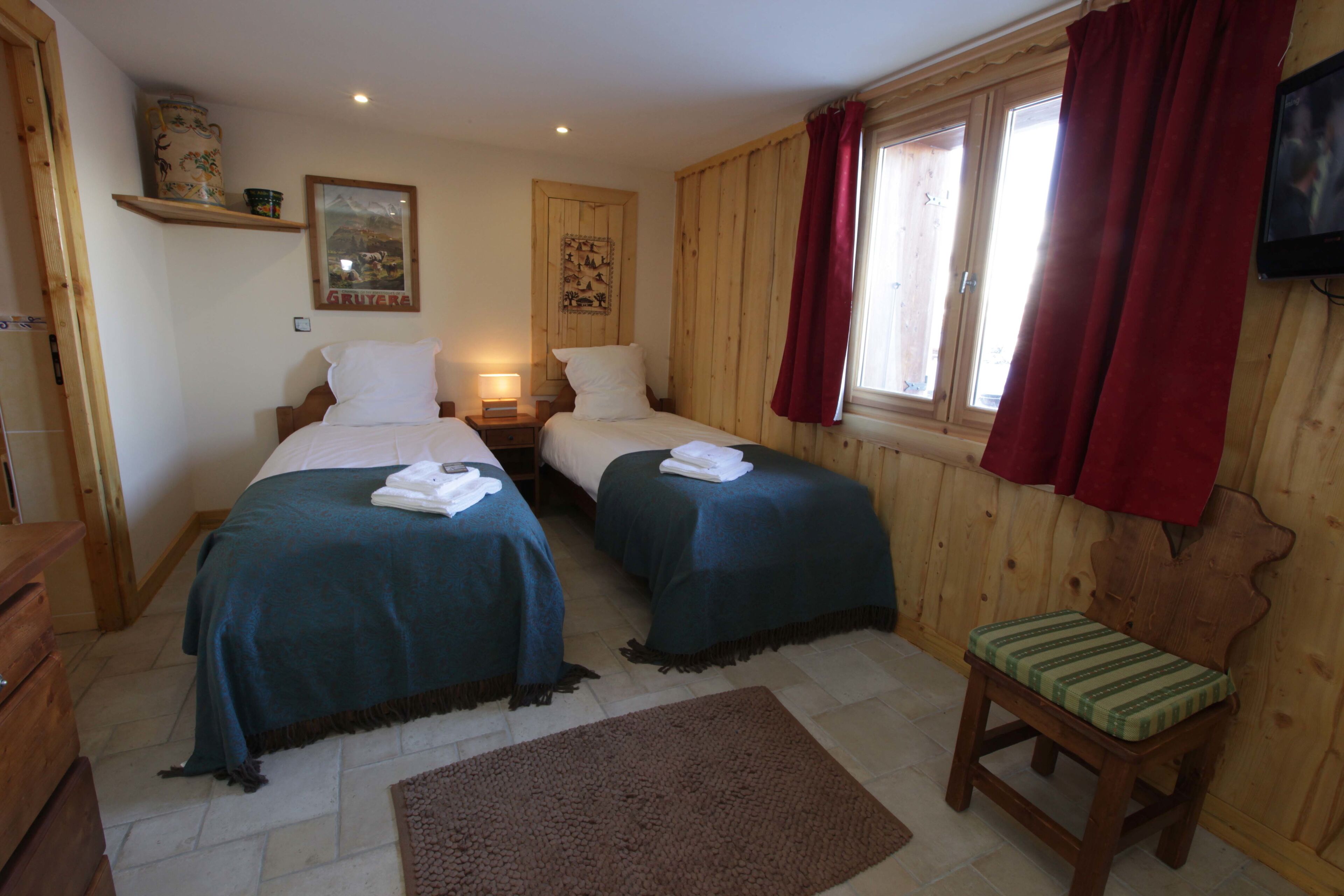 A room with two beds, a wooden chair, a small table, and a television on the wall.