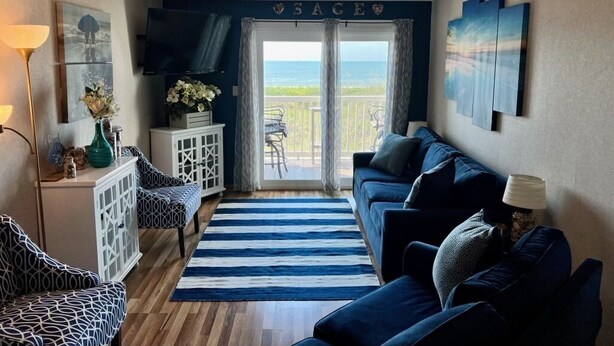 A living room with a view of the ocean, a blue couch, a white cabinet, and a TV on the wall. - 2 BR, 2 Bath, Oceanfront-First Floor-Condo A6-Dog Friendly-Wifi - NO-SMOKING! (North Myrtle Beach)