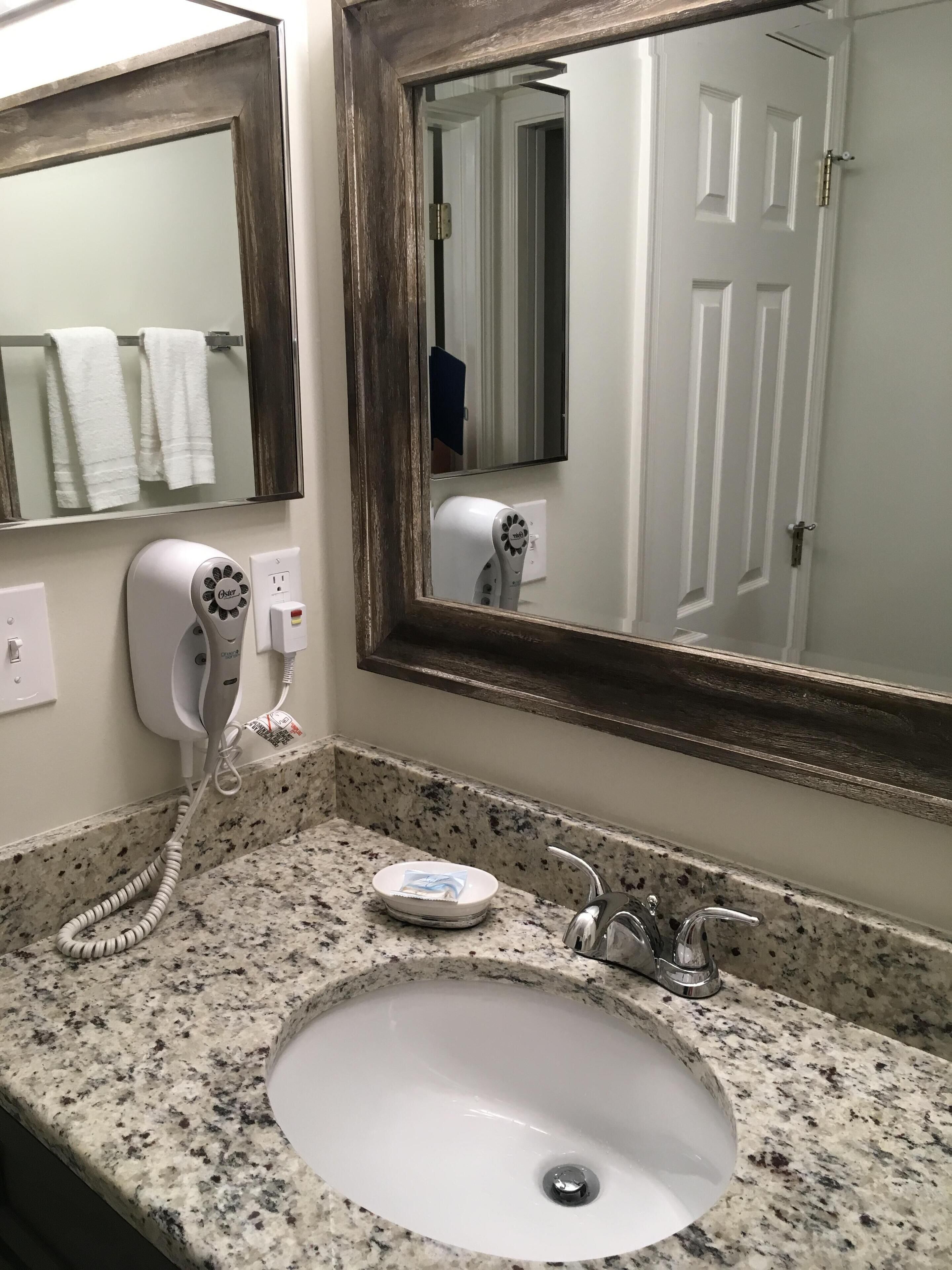 A bathroom with a granite countertop, a white sink, a hairdryer, and a mirror.