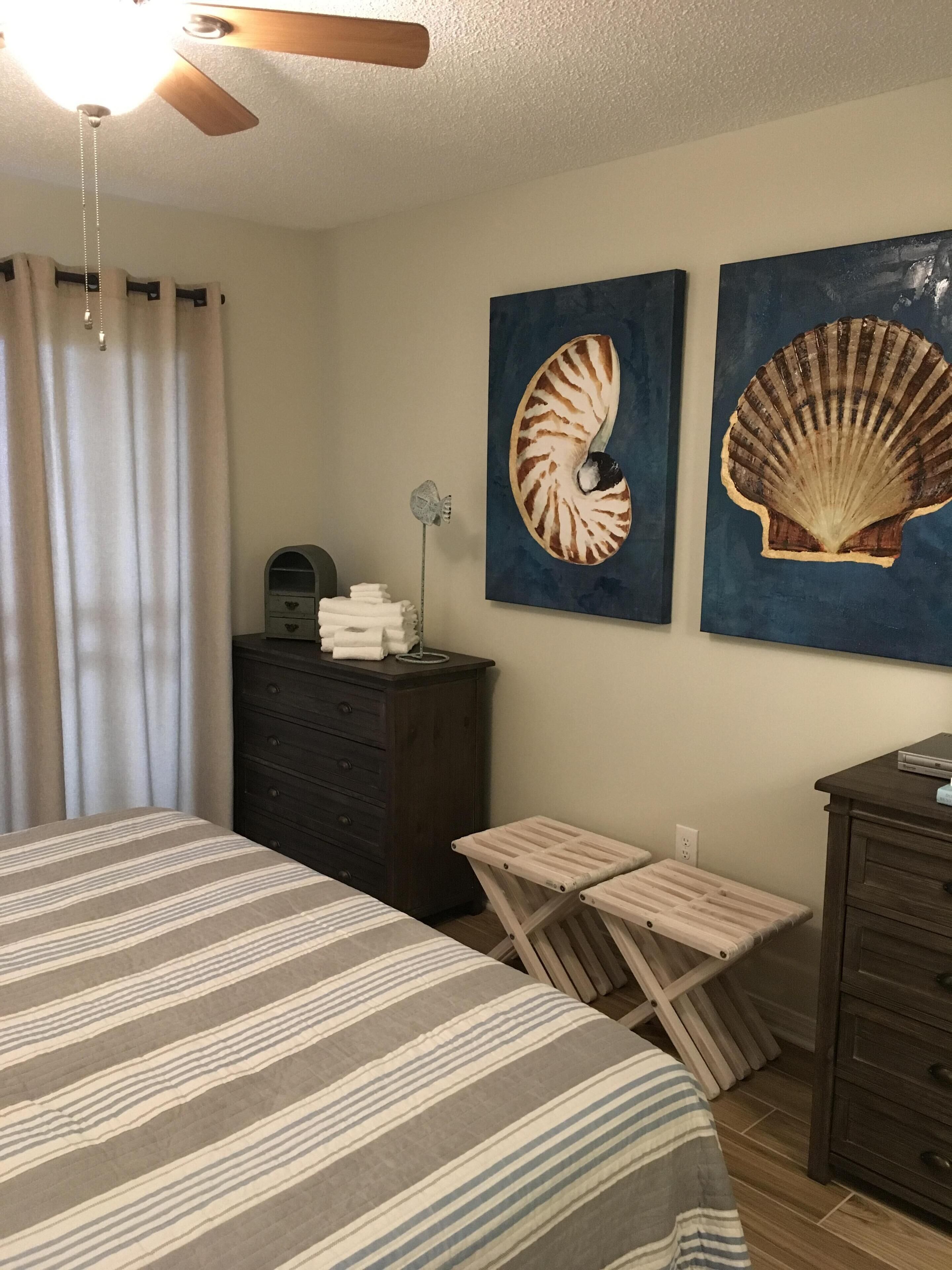 A bedroom with a bed, a dresser, a desk, and two wall-mounted paintings.