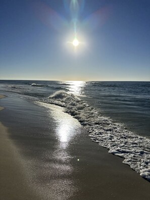 Una spiaggia con la luce del sole riflessa sulla sabbia bagnata e onde leggere.