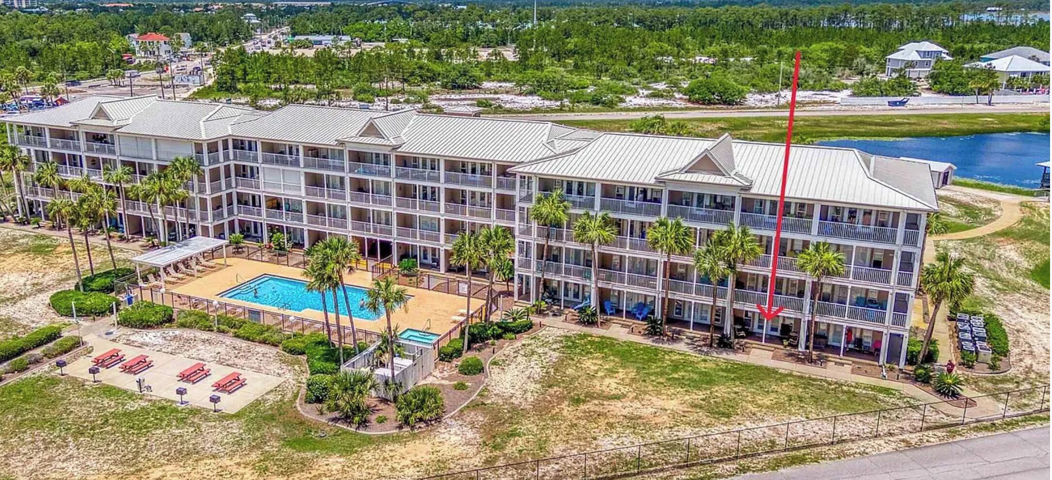 Un hôtel à plusieurs étages doté d’une piscine, entouré de palmiers et offrant une vue sur une étendue d’eau.