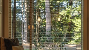 Une fenêtre avec des stores, un canapé avec des coussins et une vue sur des arbres et un immeuble.