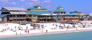 A beachside hotel with multiple green-roofed buildings, a sandy beach, and a pier.