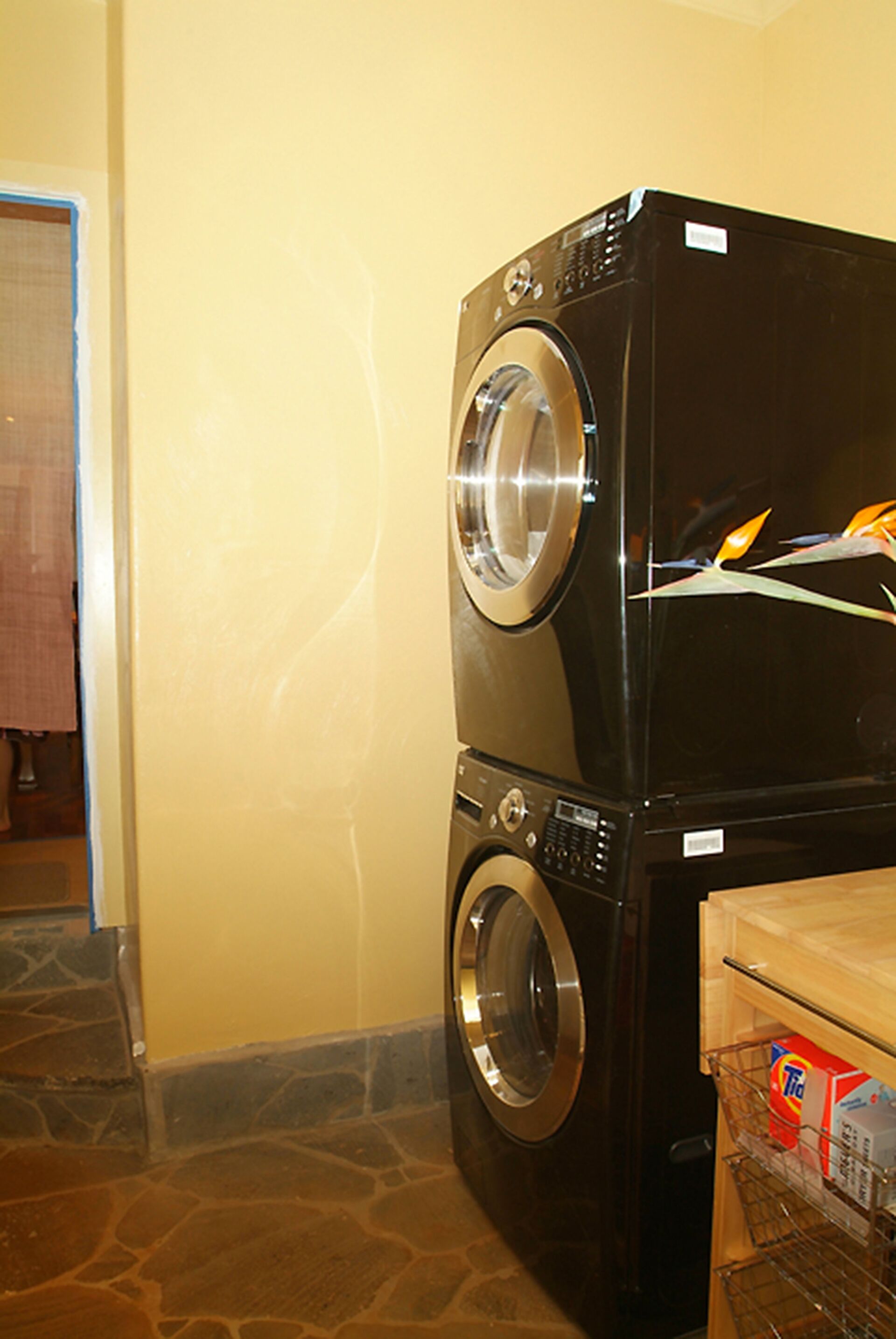 A black front-loading washing machine in a room with a stone floor and a yellow wall.