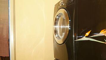 A black front-loading washing machine in a room with a stone floor and a yellow wall.