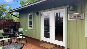 A green house with a patio area featuring a grill, outdoor seating, and a sign that reads "The Artists House Please Remove Your Shoes".