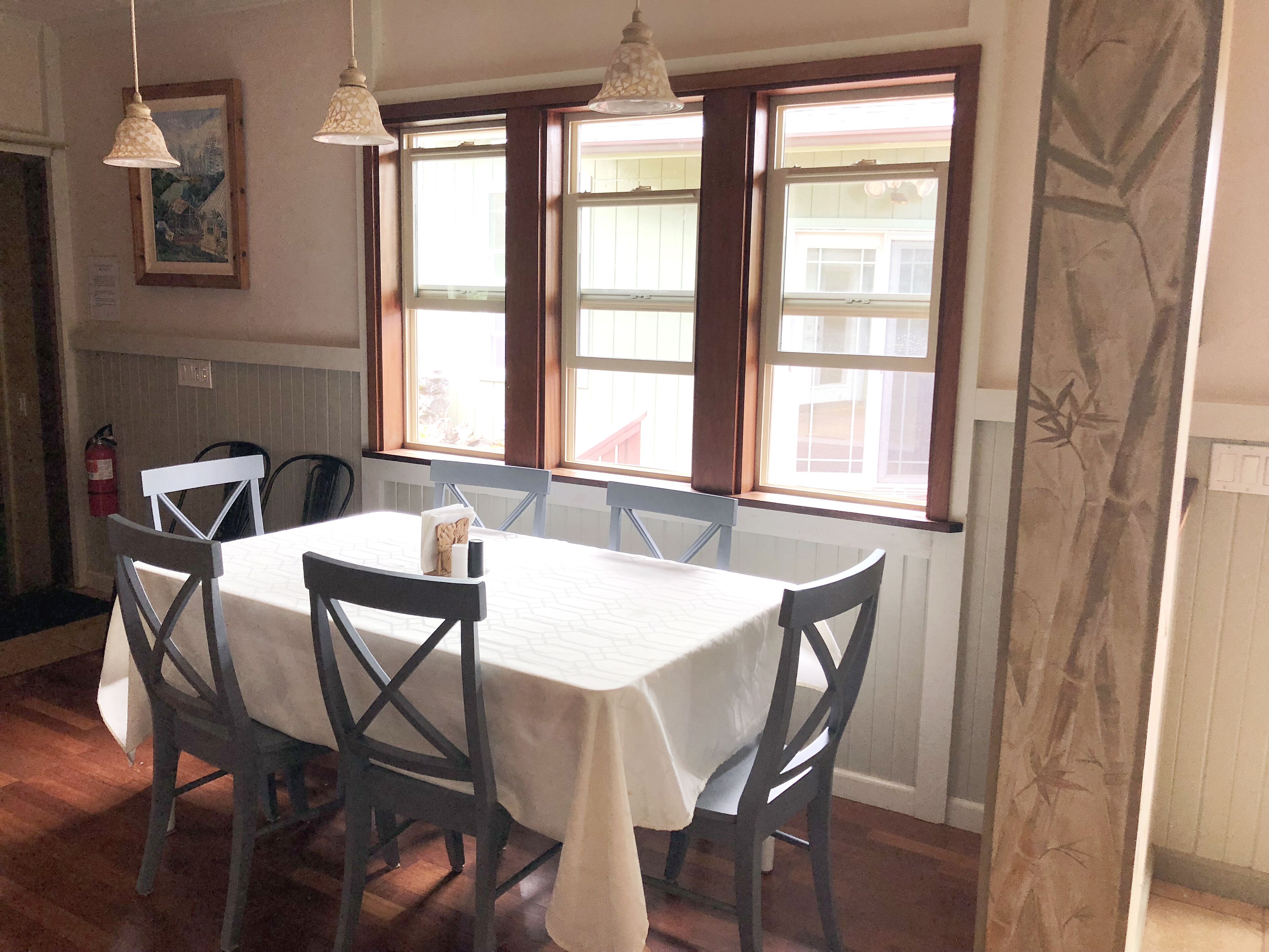 A dining area with a table set for four, wooden chairs, pendant lights, and a window with a view of buildings.
