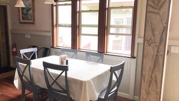 A dining area with a table set for four, wooden chairs, pendant lights, and a window with a view of buildings.