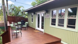 Een overdekte patio buiten met een houten terras, een barbecue en een eethoek met stoelen en een tafel.