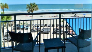 Uma varanda com vista para a praia, espreguiçadeiras e uma mesa.
