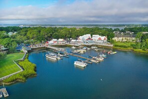 A marina with boats docked, a waterfront building with multiple levels, and a dock extending into the water.