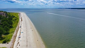Une plage côtière avec un rivage sablonneux, quelques personnes et un bateau qui laisse une vague derrière lui dans l’eau.