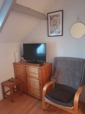 Una sala de estar acogedora con un aparador de madera, un televisor de pantalla plana, un sillón gris, un taburete de madera pequeño y una obra de arte floral enmarcada en la pared.