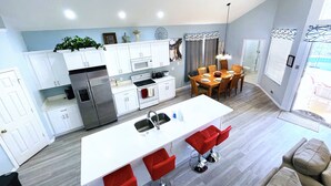 A modern kitchen with white cabinets, a central island with red bar stools, and a dining area with wooden chairs. - 6 Bed/Pool/Spa/Internet/gameRoom, 3.5 Miles to Disney,Gated Resort communities (Kissimmee)