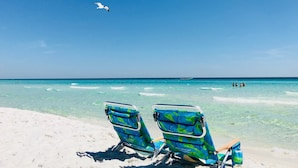 Deux chaises de plage au motif tropical, placées sur une plage de sable fin, bordée d’une eau turquoise et cristalline.