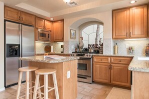 Enjoy cooking in this kitchen with a kitchen island and bar stools, featuring a decorative archway and sign.