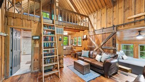 Amplia habitación estilo loft con cama alta, una gran estantería de madera, sofá de cuero y zona de comedor.