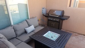 Un espacio exterior con mobiliario de jardín, incluyendo un sofá, una mesa, una parrilla y una ventana.
