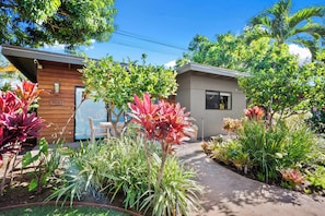 Une villa moderne avec une façade en bois, une petite dépendance attenante et un jardin bien entretenu, agrémenté de diverses plantes et d’un sentier.