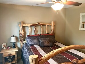 A bedroom with a rustic wooden headboard, a bed with patterned bedding, a nightstand with a lamp, and a ceiling fan. - Luxury Duck Creek Log Cabin, ATV Trails Access, Near Zion, Bryce, & Brian Head (Duck Creek Village)
