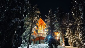 Eine schneebedeckte Lodge mit einem markanten, orange beleuchteten Turm, umgeben von hohen Kiefern.