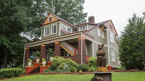 Une grande maison à deux étages, dotée d’un porche imposant et d’un escalier menant à l’étage supérieur.