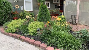 Une maison dotée d’un porche à l’avant, d’un patio couvert et d’un jardin où poussent diverses plantes et fleurs.