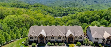 A hotel with a central building and two wings, surrounded by lush greenery and mountains.