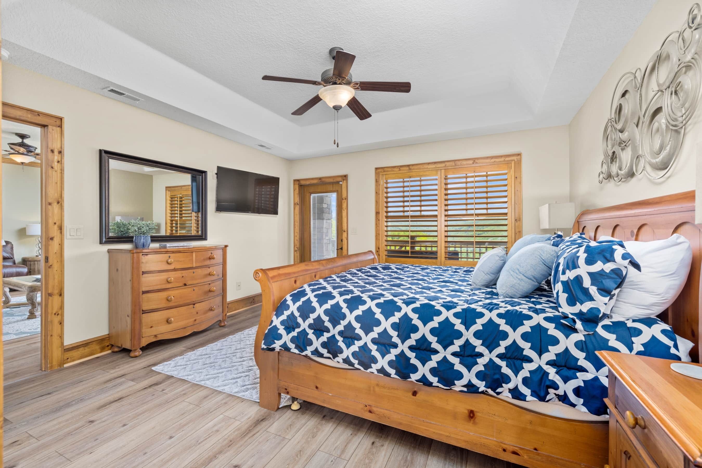 A bedroom with a wooden bed, a ceiling fan, a dresser, a mirror, and a window with blinds.