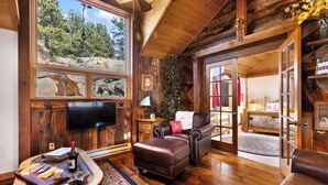 Interior acolhedor de uma cabana, com teto de madeira, lareira, sofá de couro e área de jantar com mesa posta para refeição.