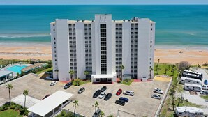 Un hôtel de grande hauteur avec une entrée principale, de nombreux espaces de stationnement et une vue sur la plage et l’océan.