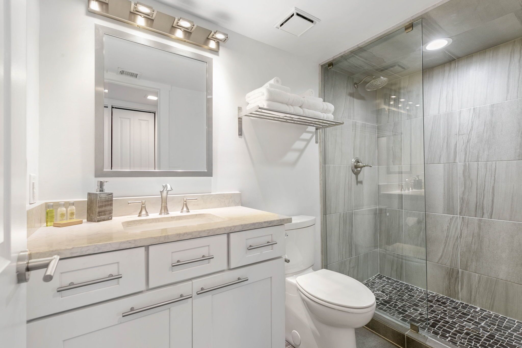 A modern bathroom with a glass shower enclosure, a white toilet, and a vanity with a mirror and lights.