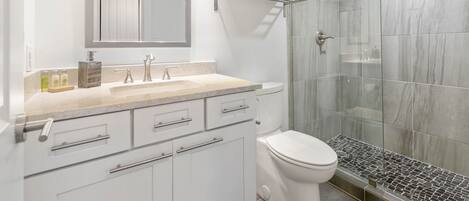 A modern bathroom with a glass shower enclosure, a white toilet, and a vanity with a mirror and lights.