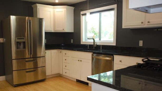 A modern kitchen with stainless steel appliances, white cabinetry, and a black countertop.