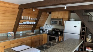 Une cuisine dotée de plans de travail en granit, d’armoires en bois, d’un évier en acier inoxydable, d’un four à micro-ondes, d’une cuisinière et d’un réfrigérateur.