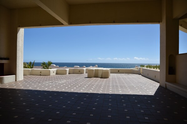 An outdoor terrace with a view of the ocean, featuring a tiled floor and several seating areas.