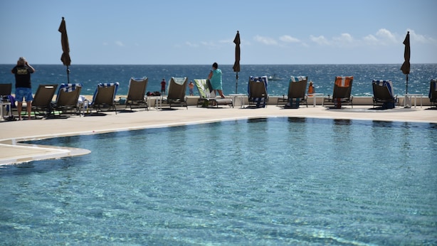 Zona de piscina con sillones de descanso y sombrillas, con vista al océano azul y despejado.