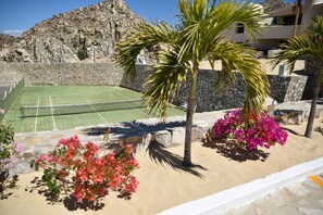 Un court de tennis avec un mur en pierre en arrière-plan, des palmiers et des fleurs de bougainvillier.