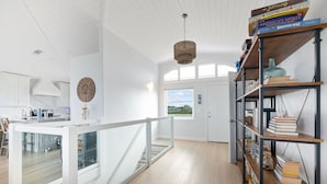 A spacious kitchen with white cabinetry, a dining area with a glass partition, and a bookshelf filled with books and decorative items.