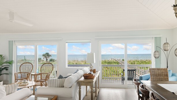 A spacious living room with a view of the ocean, furnished with a sofa, chairs, and a dining table.