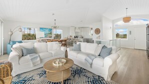 A spacious living room with white sofas, a coffee table, and a dining area with chairs and a table.