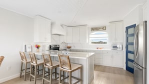 A modern kitchen with white cabinetry, a large island with bar stools, a stainless steel refrigerator, and a window providing natural light.