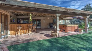 Un patio couvert avec un coin bar, des sièges d’extérieur et un jacuzzi.