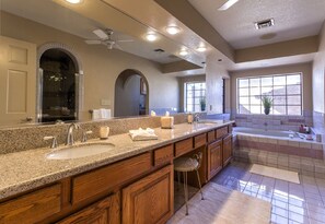 A modern bathroom with a large vanity, two sinks, a bathtub, and a ceiling fan.