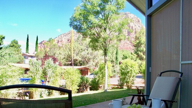 A patio with a table set for two, a chair, and a view of a mountainous landscape.